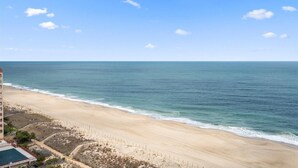 Una playa con vista despejada al océano, una orilla arenosa y un edificio con piscina al frente.