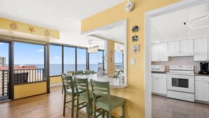 Un comedor con vistas al océano, una cocina con armarios blancos y un balcón con barandilla.