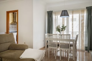 A room with a sofa, dining table, chairs, a hanging light fixture, and a window with curtains.