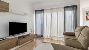 Una sala moderna con un televisor de pantalla plana, mueble de entretenimiento de madera y un sofá color beige.