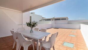 Una terraza con una mesa y sillas blancas, una planta en maceta y vistas a edificios.
