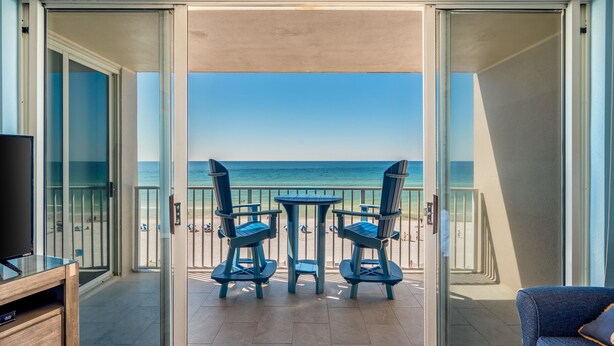 Un balcón con mesa y sillas, un televisor y vista a la playa.