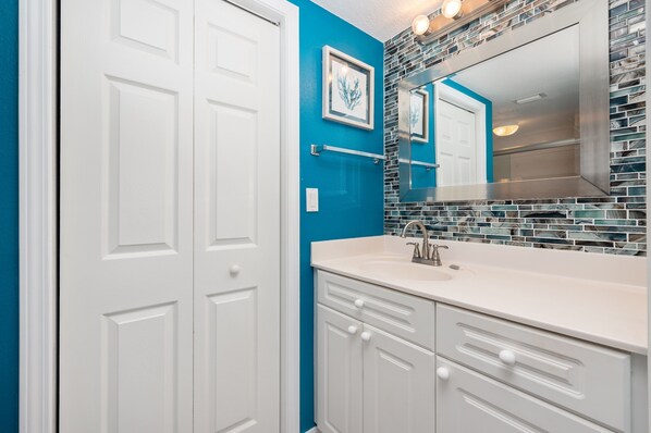 Un baño con armarios blancos, una pared azul decorativa, salpicadero de azulejos y un espejo grande.