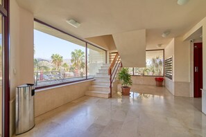 Zona interior àmplia amb una escala que condueix a un nivell superior, un safataire i plantes en testos.