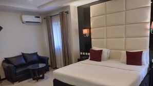 Ein Hotelzimmer mit einem großen Bett, einem schwarzen Ledersofa, einem kleinen runden Tisch und einer Klimaanlage an der Wand.