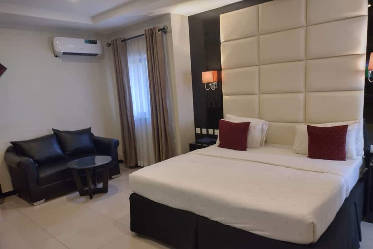 A hotel room with a large bed, a black leather sofa, a small round table, and an air conditioning unit on the wall.