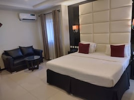 Una habitación de hotel con una cama grande, un sofá de cuero negro, una mesita redonda y un equipo de aire acondicionado en la pared.