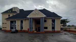 Ein Gebäude mit der Aufschrift 'ADIGA', das einen schlichten Baustil mit Flachdach und einem mittleren Eingang, der von zwei Säulen betont wird, aufweist.