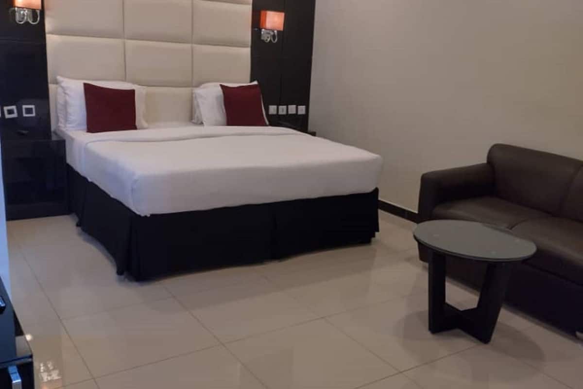 A hotel room with a large bed, a sofa, a small table, and a nightstand.