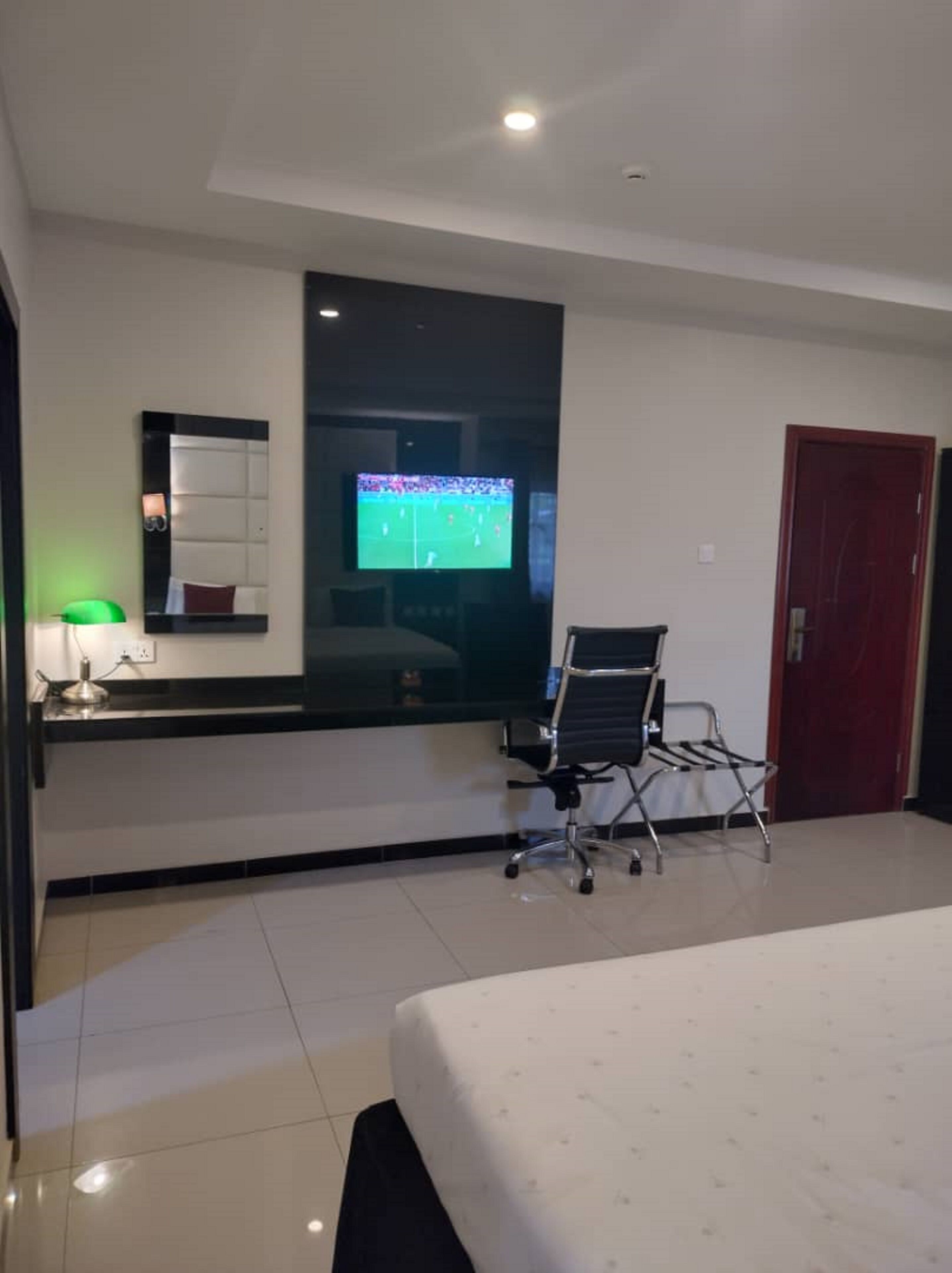 A modern hotel room with a large bed, a desk with a chair, a flat-screen TV, a mirror, and a red door.