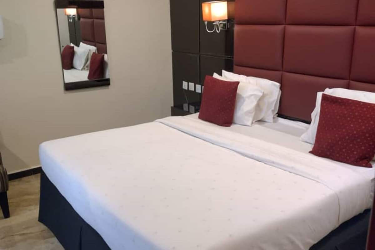 A hotel room with a large bed, a headboard, a nightstand, and a mirror on the wall.