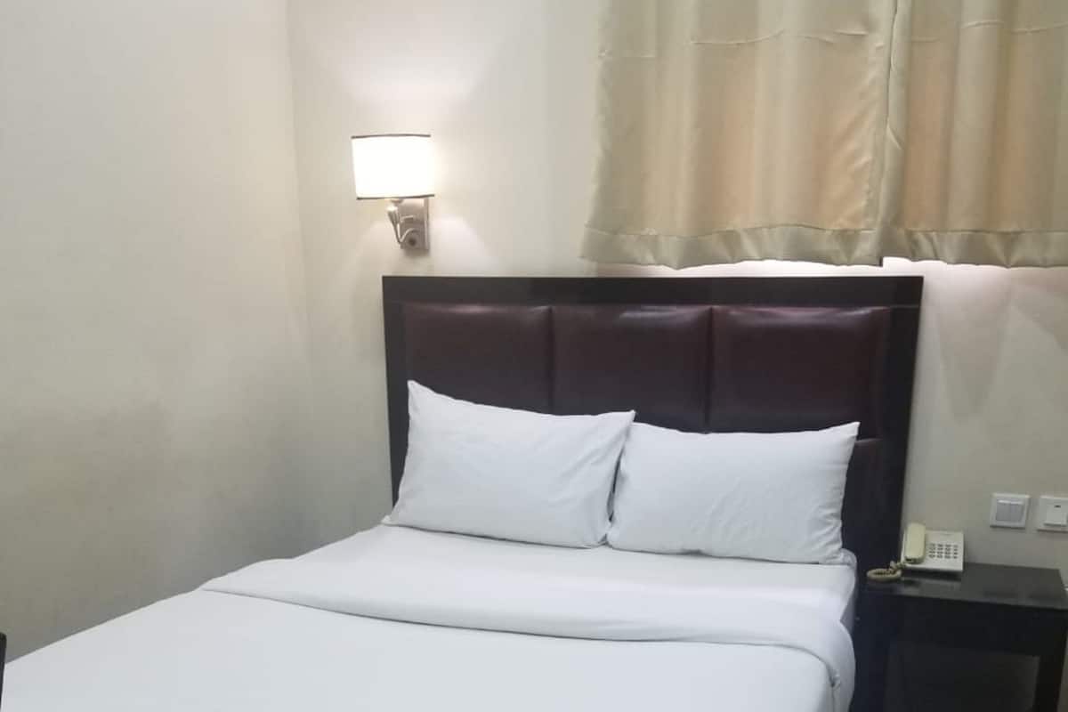 A neatly made bed with white linens, a dark headboard, and a bedside table with a lamp.