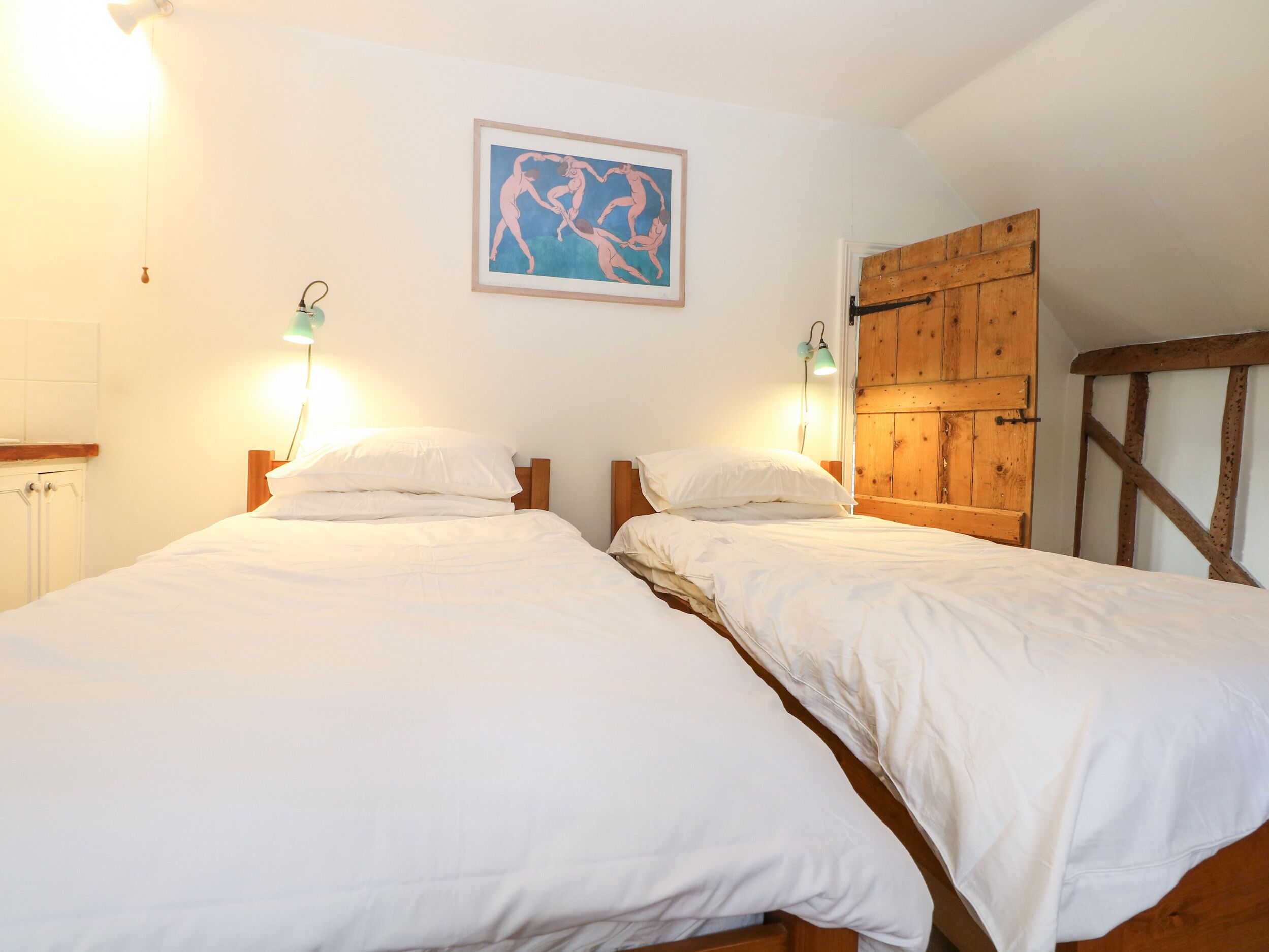 Una habitación con dos camas individuales, un armario de madera, una obra de arte enmarcada en la pared y un pequeño escritorio con lámpara.