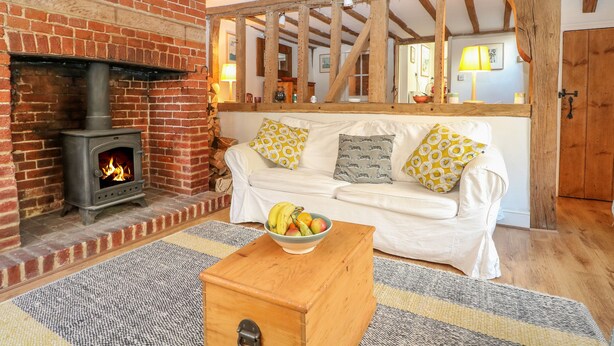 A cozy living room with a brick fireplace, wooden beams, a white sofa with patterned cushions, and a fruit bowl on a wooden table. - 48 Polecat Cottages (Lewes)