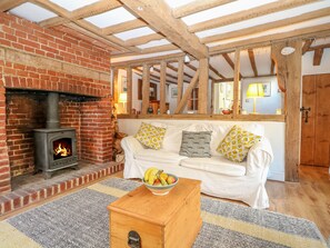 A cozy living room with a brick fireplace, wooden beams, a white sofa with patterned cushions, and a fruit bowl on a wooden table. - 48 Polecat Cottages (Lewes)