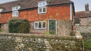 A two-story brick house with a tiled roof, a stone wall in the foreground, and a small garden area with shrubs and a tree. - 48 Polecat Cottages (Lewes)