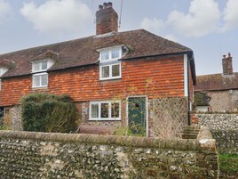 A two-story brick house with a tiled roof, a stone wall in the foreground, and a small garden area with shrubs and a tree.