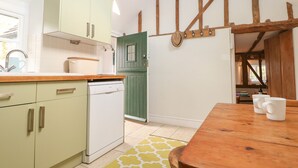A kitchen with light green cabinets, a wooden countertop, a dishwasher, and a dining area with a wooden table and chairs. - 48 Polecat Cottages (Lewes)