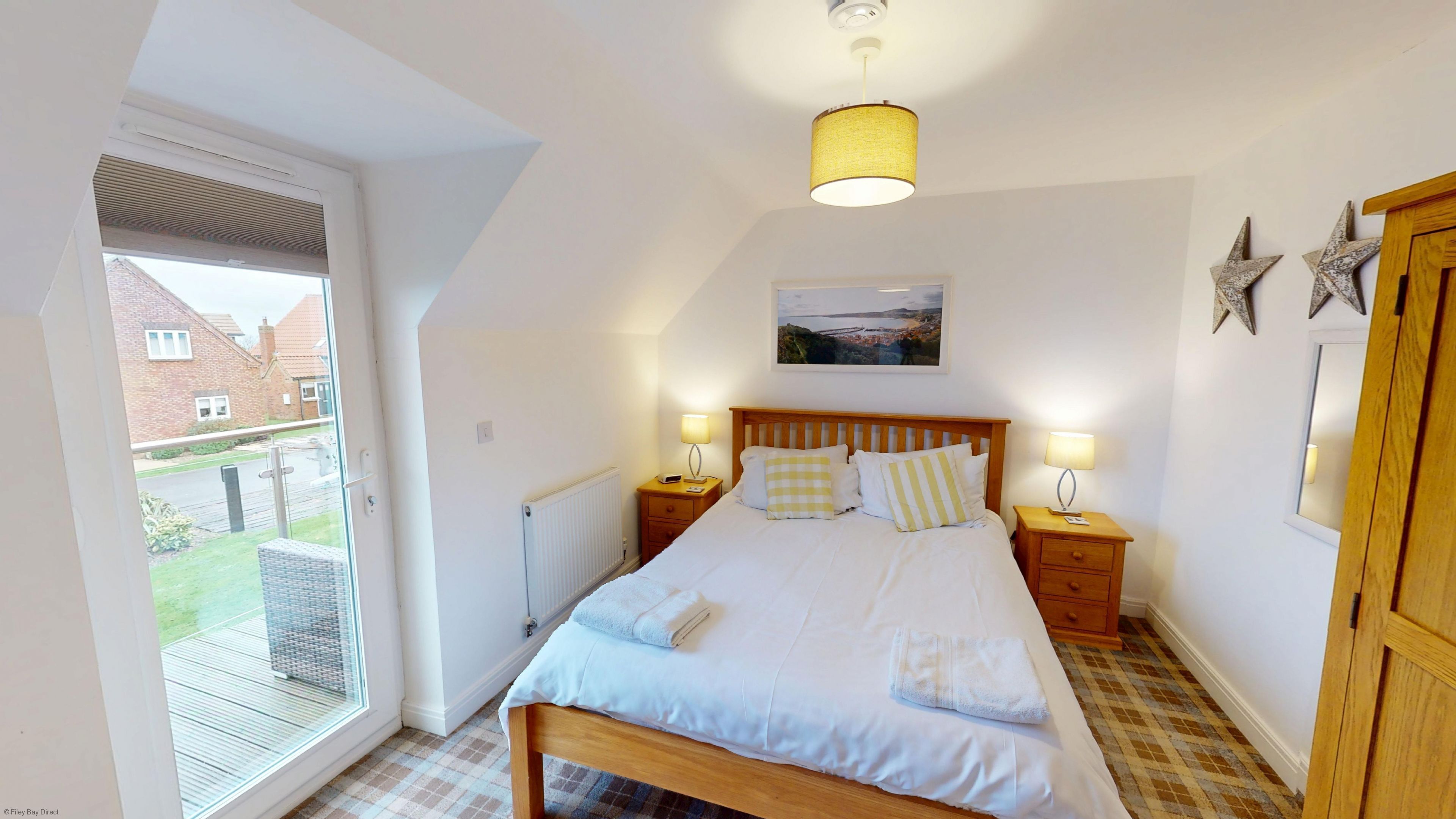A bedroom with a bed, two bedside tables, a window, a radiator, and a picture on the wall.