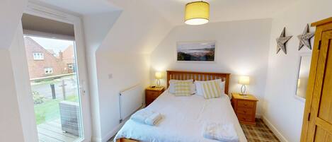 A bedroom with a bed, two bedside tables, a window, a radiator, and a picture on the wall.