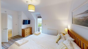 Un dormitorio con una cama grande, un televisor de pantalla plana montado en la pared, un aparador de madera y un cuadro en la pared.