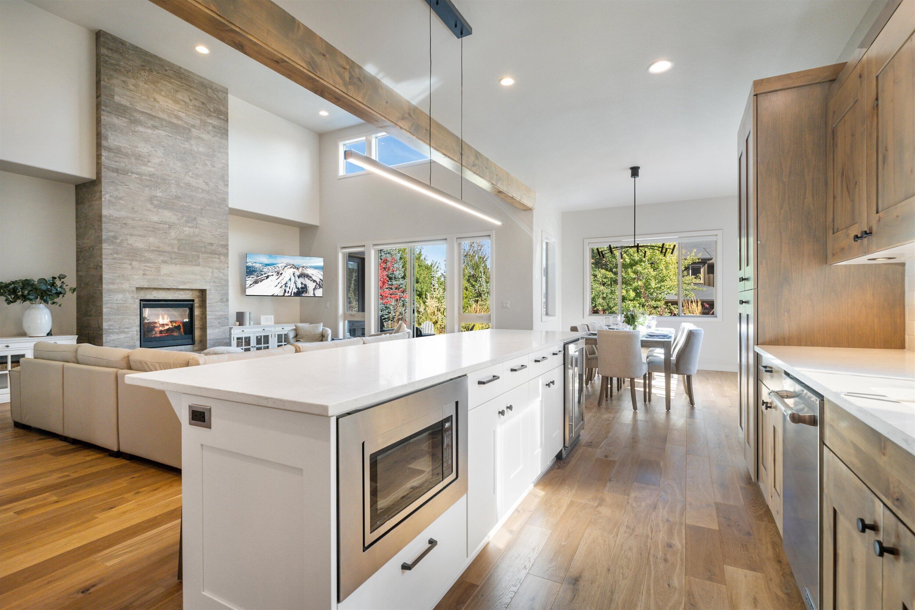 Una cocina moderna con una isla grande, vigas de madera y un comedor con luz natural.