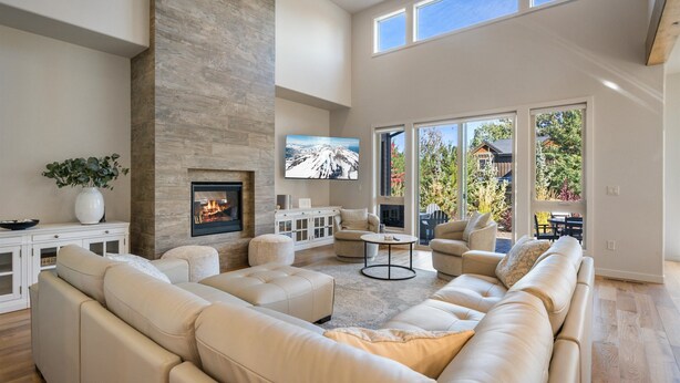 A spacious living room with a fireplace, comfortable seating, and large windows offering a view of the outdoors. - Hummingbird House | Luxury | River | Spa (Deschutes County)