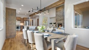 A modern kitchen with stainless steel appliances, a dining area with a wooden table and chairs, and a fireplace. - Hummingbird House | Luxury | River | Spa (Deschutes County)