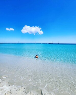 A beach with clear turquoise water and a person swimming.