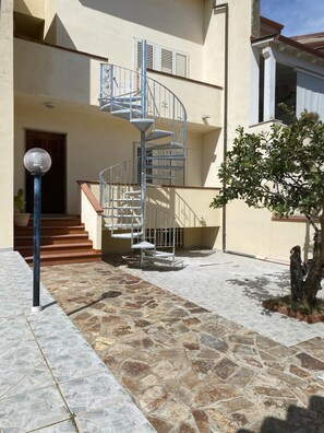 A spiral staircase leading to a second floor, a stone-tiled courtyard, and a potted plant. - Spacious holiday home near the sea with courtyard perfect for families & friends (Cooperativa Phiniscollis)