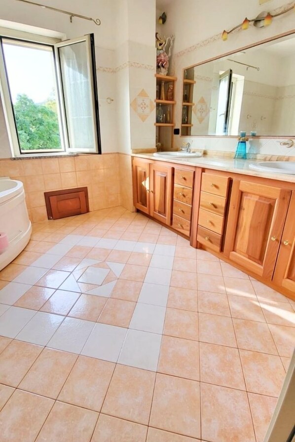 A bathroom with a bathtub, wooden cabinets, a large mirror, and a window. - Spacious holiday home near the sea with courtyard perfect for families & friends (Cooperativa Phiniscollis)