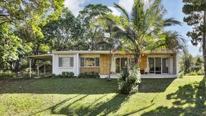 Ein eingeschossiges Haus mit einer Veranda, einem kleinen Garten und einer Palme.