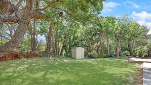 Ein gepflegter Rasen mit einer kleinen Gartenhütte, umgeben von alten Bäumen und blauem Himmel.