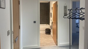 Un couloir avec une porte en bois, un porte-manteau et une salle de bain visible au fond.