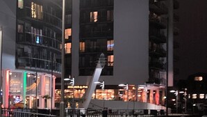 Un bâtiment moderne à étages, doté de grandes fenêtres, entouré d’une clôture et éclairé par des lampadaires.