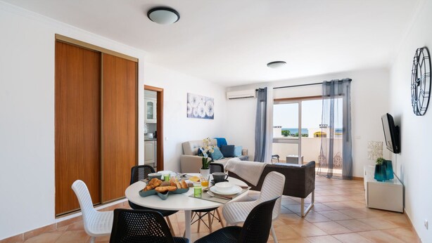 A dining area with a round table, black chairs, and a view of the sea through a balcony. - Odissi Apartment, Vilamoura, Algarve (Quarteira)
