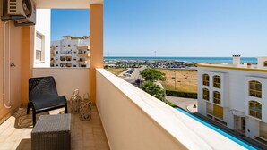 A balcony with a view of the sea, a chair, a small table, and a pool. - Odissi Apartment, Vilamoura, Algarve (Quarteira)