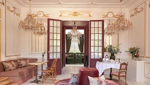 A luxurious room with a red velvet sofa, a round ottoman, a dining table with chairs, and a chandelier. - Château Léognan, Domaine viticole - proche Bordeaux (Leognan)