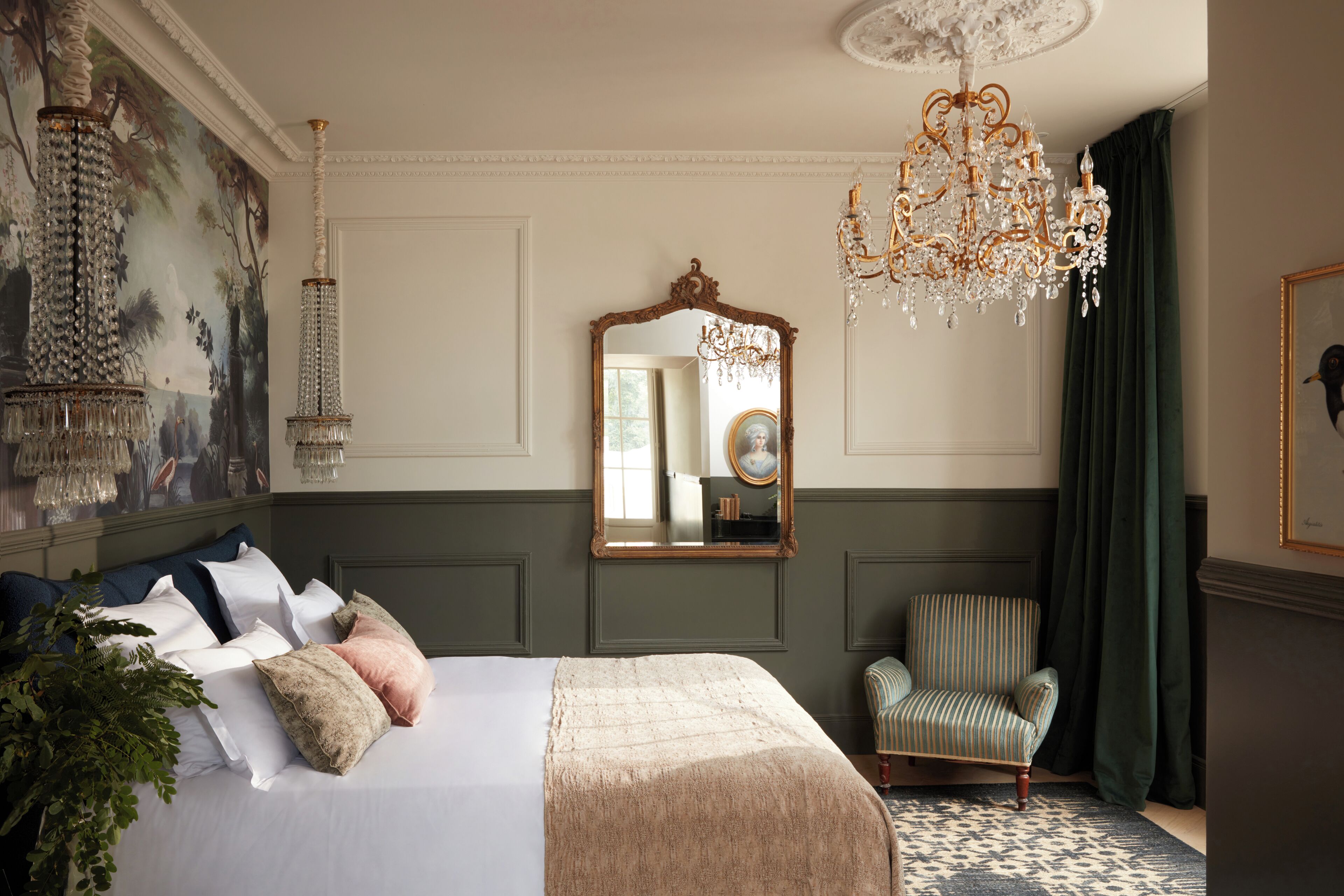 A bedroom with a large bed, a mirror, a chandelier, a chair, and a painting on the wall.