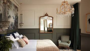 A bedroom with a large bed, a mirror, a chandelier, a chair, and a painting on the wall.