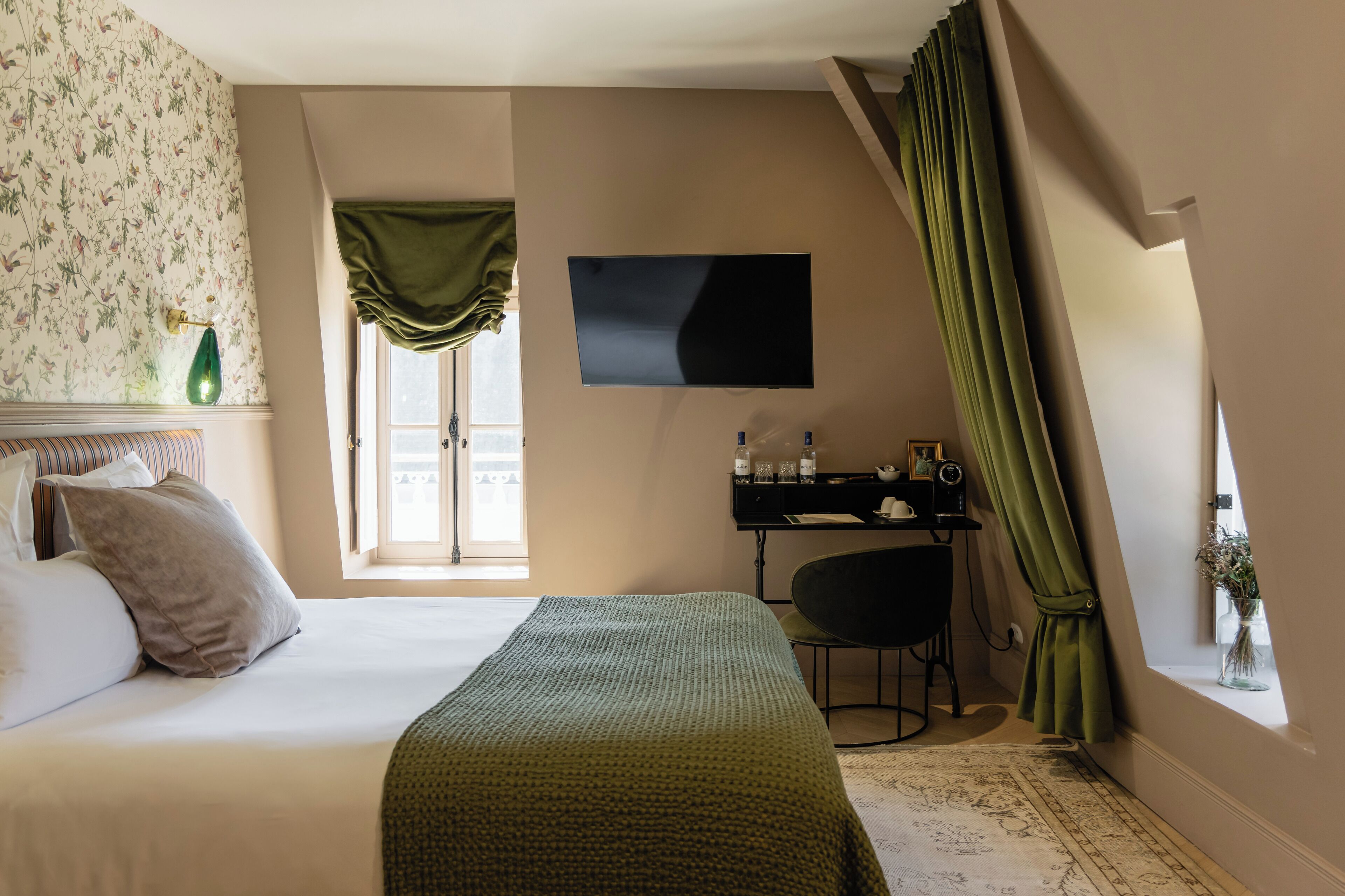 Un dormitorio con cama, escritorio, silla, televisor y ventana con cortinas.