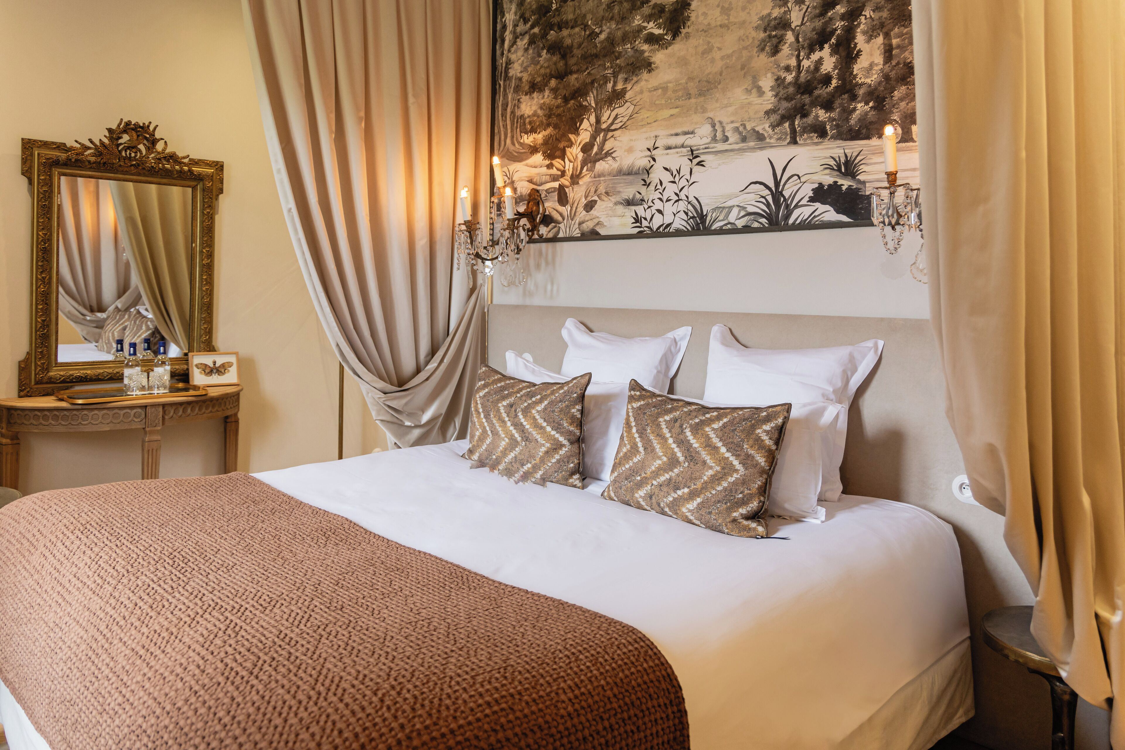 A neatly made bed with a patterned throw, a mirror with a decorative frame, and a wall tapestry.