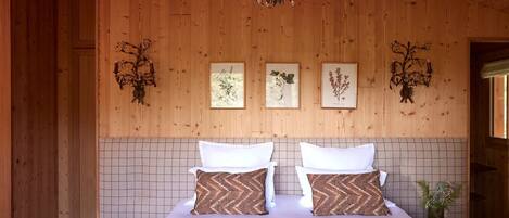 Una habitación con paneles de madera, una cama, dos impresiones enmarcadas de plantas y un candelabro.