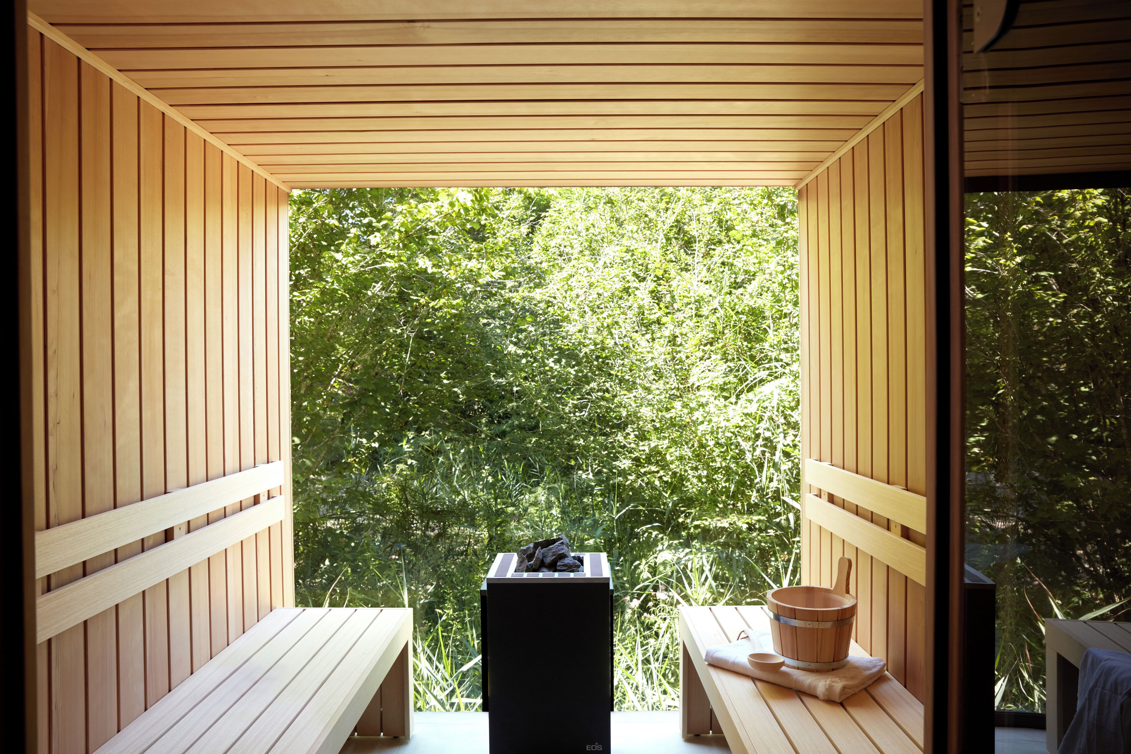 A wooden deck with a bench and a table, a black speaker, and a wooden bucket.