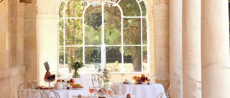 A dining area with a table set for a meal, a chandelier, and a large arched window with a view of greenery.