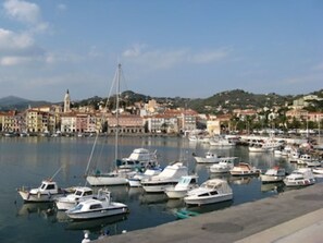 A marina with numerous boats docked, a prominent church tower, and a backdrop of colorful buildings.