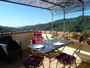 A terrace with a table set for two, surrounded by potted plants and a view of the hills.