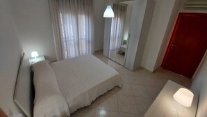 Un dormitori amb un llit, una tauleta de nit, un mirall, una porta i una làmpada.