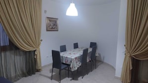 Zona de menjador amb una taula i cadires, una làmpada penjant i cortines.