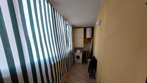 Passadís estret amb paper pintat a ratlles, una màquina de rentar i un tendal de roba.